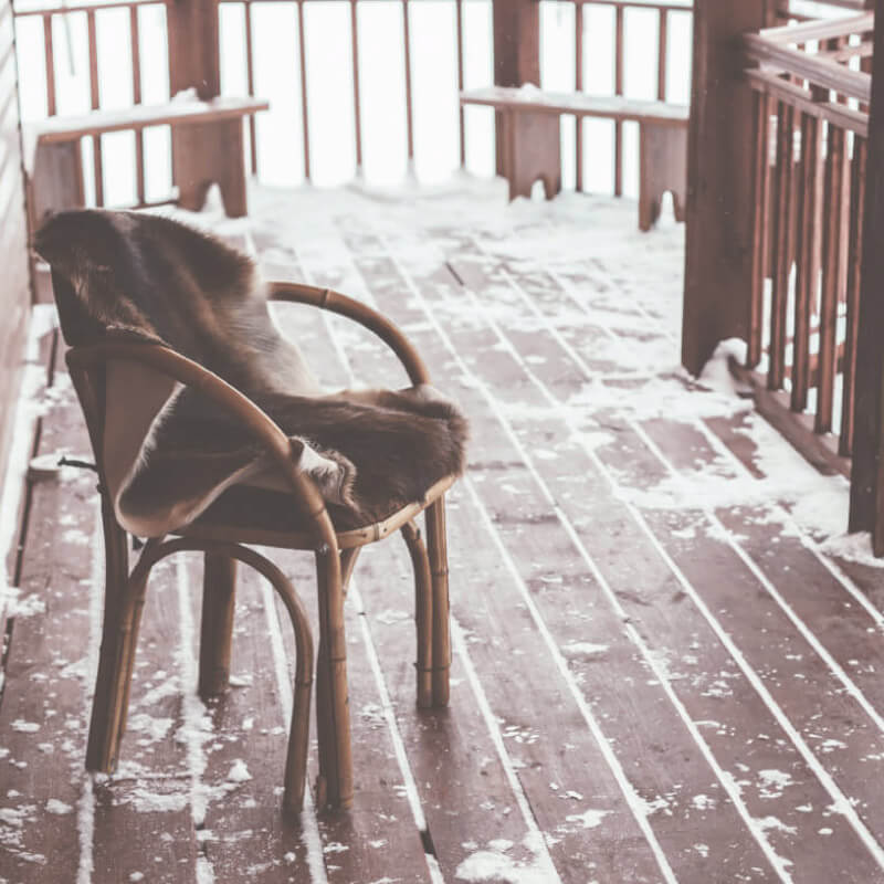 A snowy wooden terrace with a chair in the winter